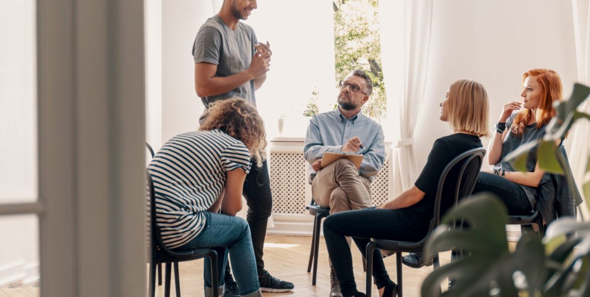 Happy hispanic man talking to his support group about his succes How Long is Alcohol Rehab?